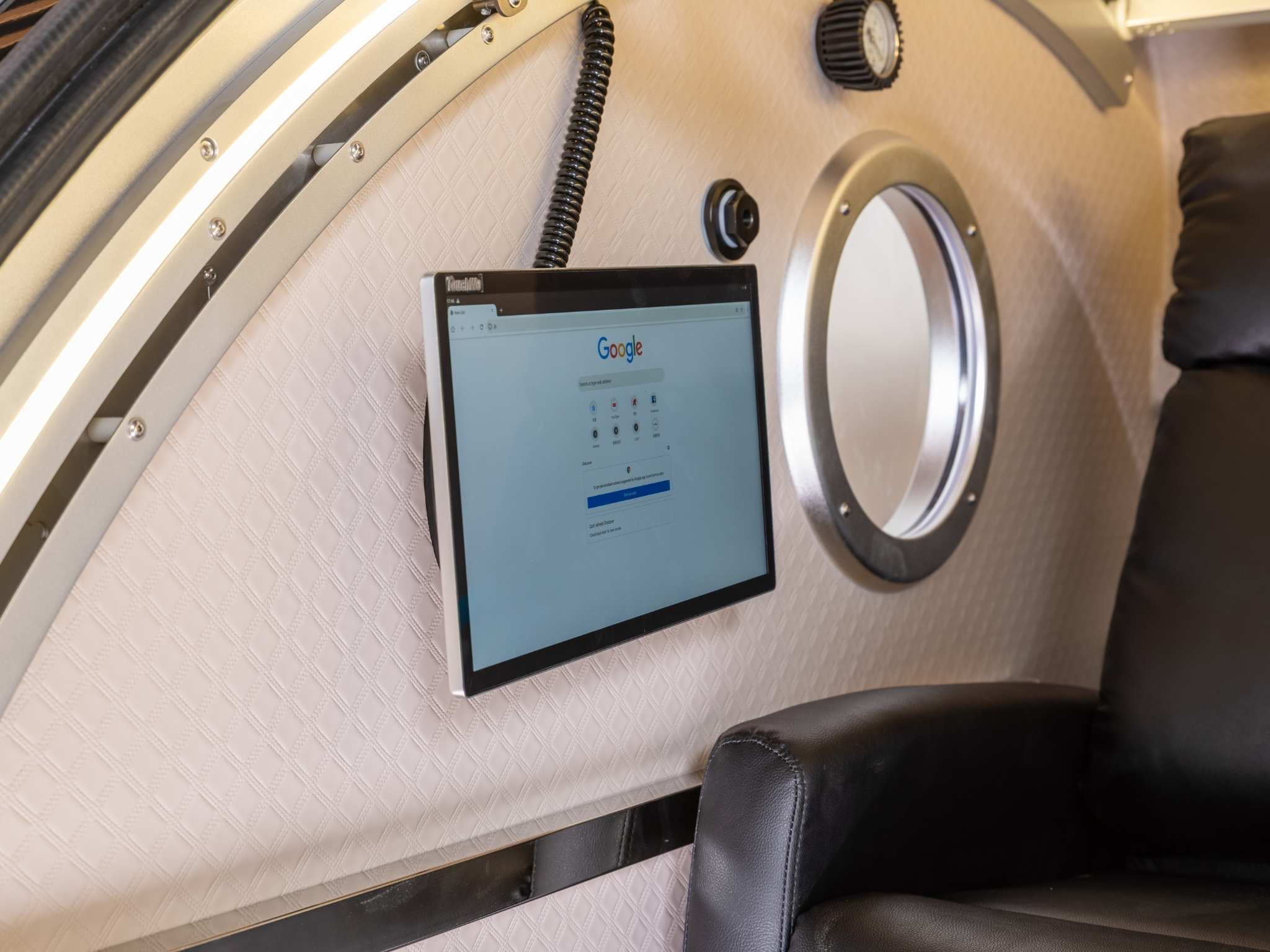 Interior of a seated hyperbaric oxygen chamber featuring a touchscreen display, observation window, and comfortable reclining chair.
