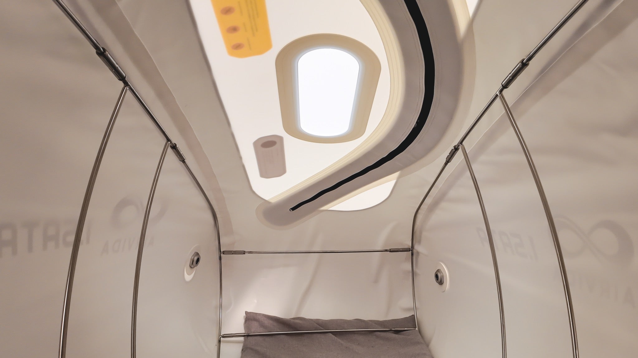 An AIRVIDA hyperbaric chamber showing a bright overhead window, sturdy support frame, air ports, and spacious padded treatment area.