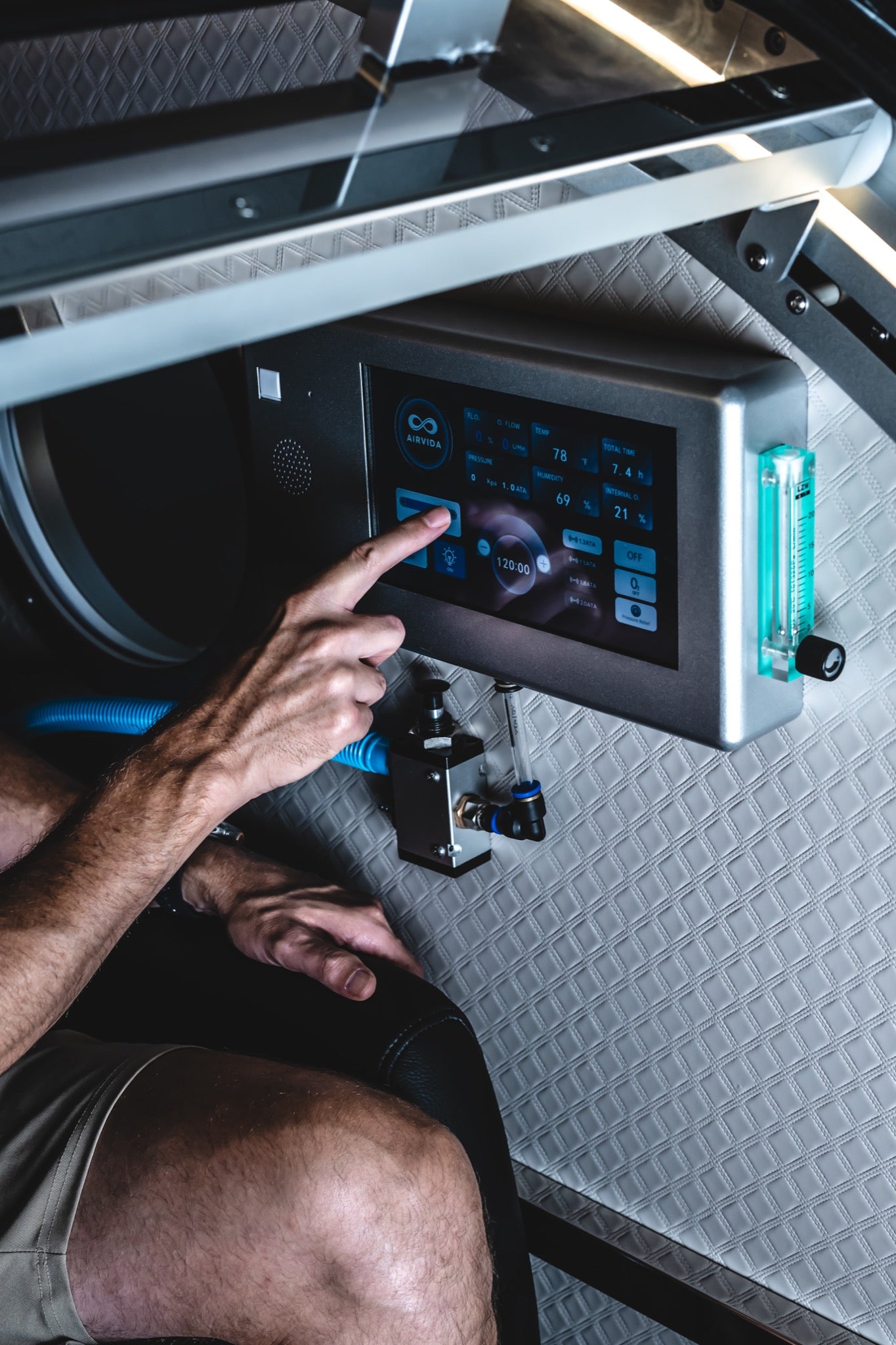 Person adjusting the touchscreen control panel inside a hard-shell hyperbaric chamber during an HBOT session.