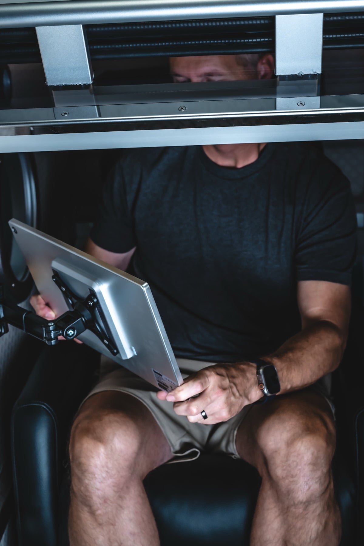 Man seated inside an Airvida hyperbaric chamber holding an adjustable tablet, with cushioned seating and metal support bars visible during a wellness session.
