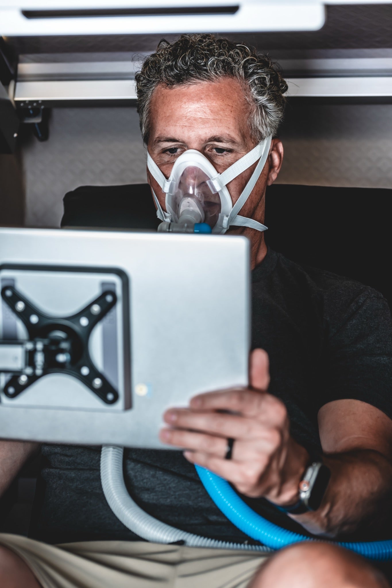 Man wearing an oxygen mask while using a tablet inside a hyperbaric chamber during an HBOT session.