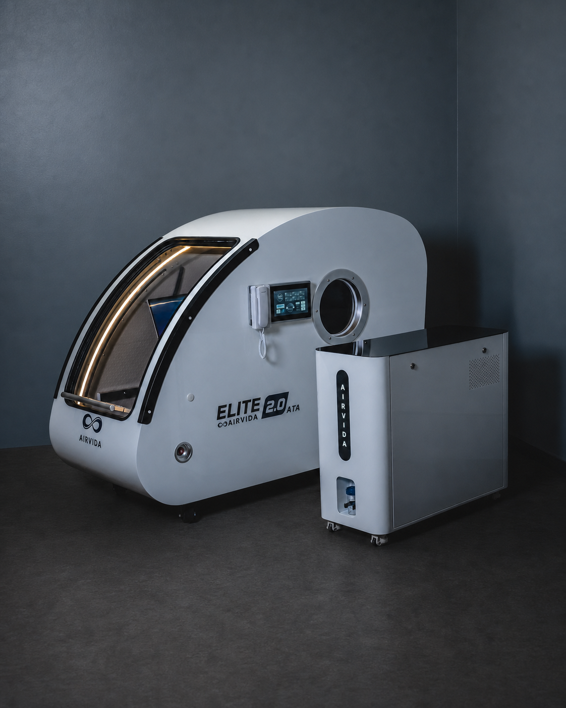 AIRVIDA Elite 2.0 ATA hard-shell hyperbaric chamber with a touchscreen, viewing port, illuminated entry, and separate oxygen control unit.