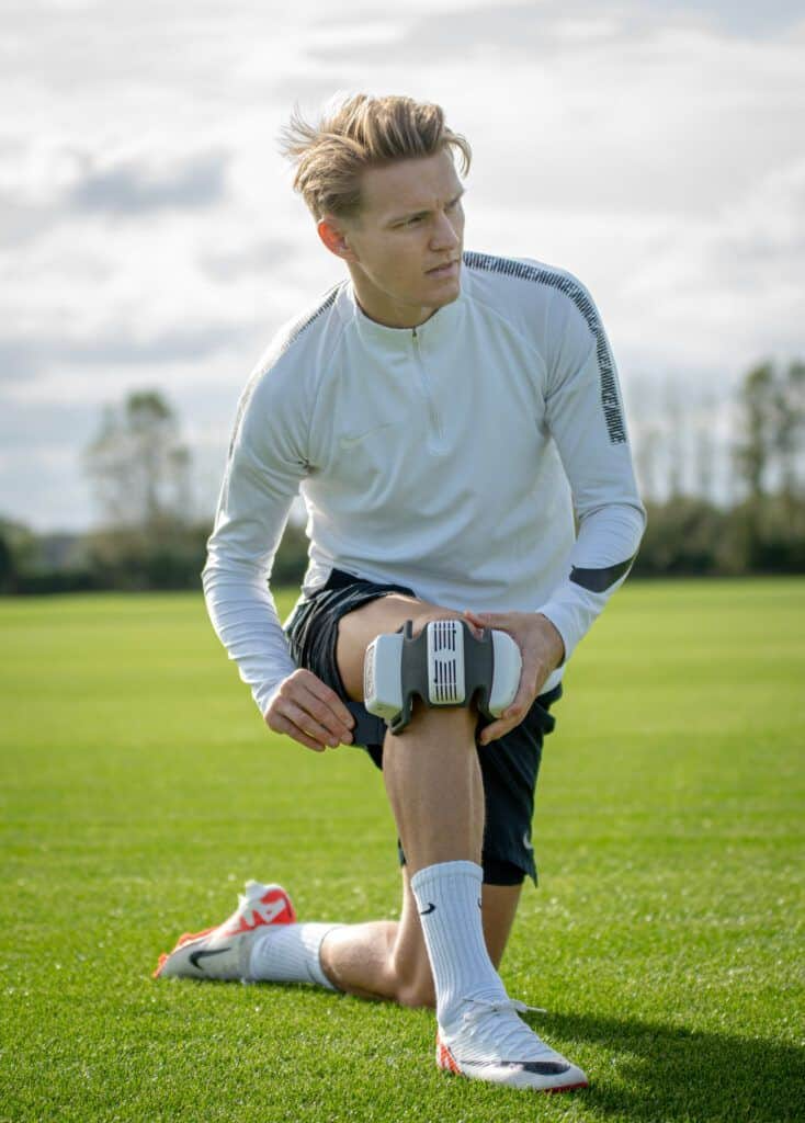 A person stretching on a grassy field wearing a FlexBeam Portable Red Light Therapy Device.