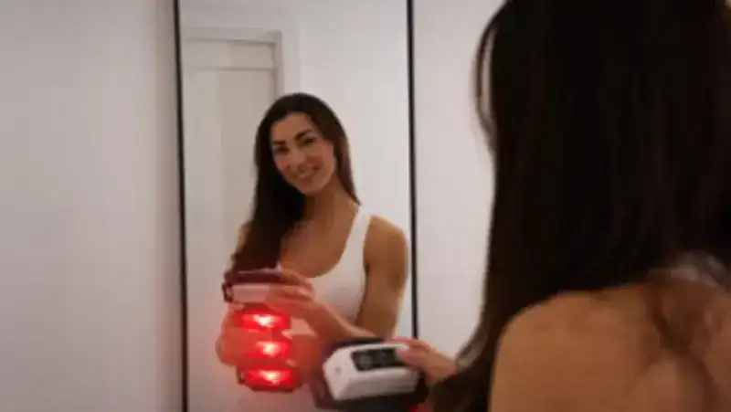 Woman using a FlexBeam Portable Red Light Therapy Device in front of a mirror
