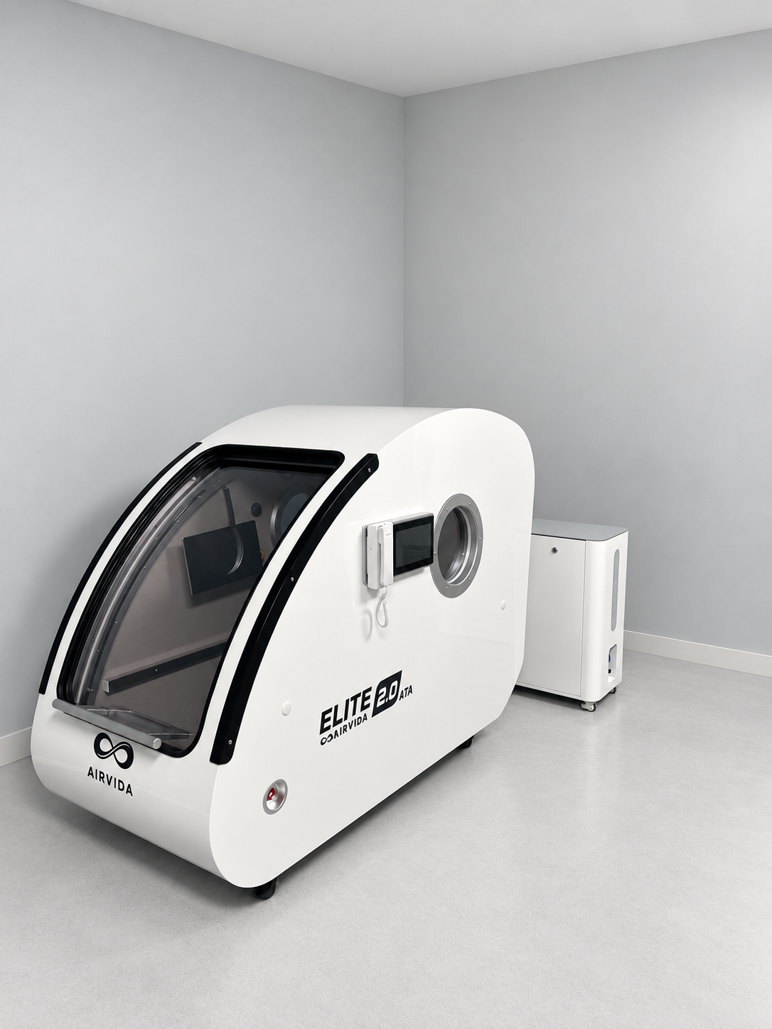 White Airvida Elite 2.0 hyperbaric chamber with clear front door, side controls, viewing port, and external oxygen system displayed in a clean modern room.