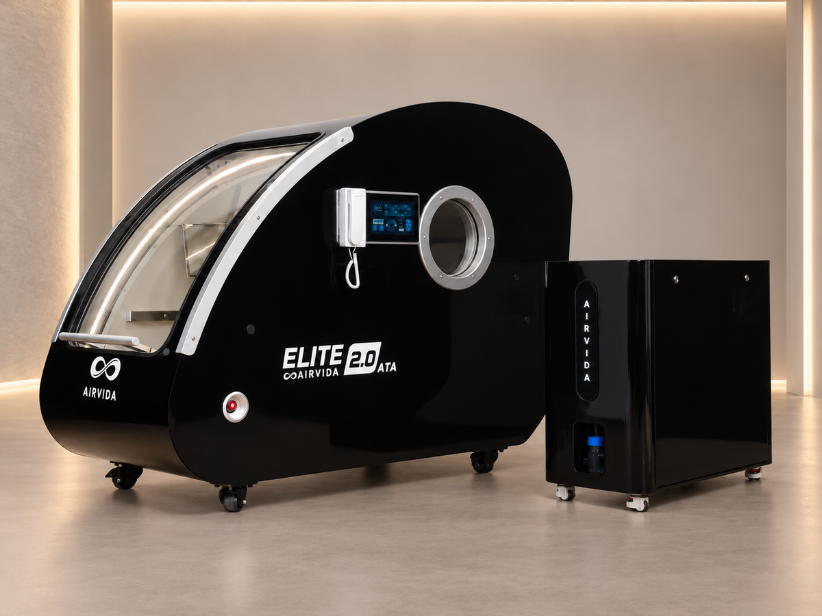 Black Airvida Elite 2.0 hyperbaric chamber with matching oxygen system, touchscreen controls, viewing port, and wheeled design in a modern wellness room.
