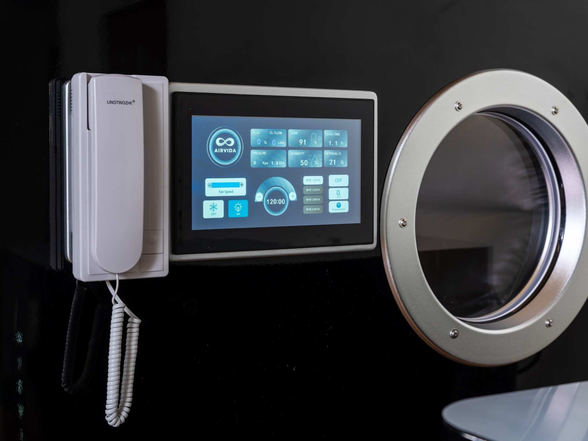 Close-up of a hyperbaric oxygen chamber touchscreen control panel, communication handset, and observation window.