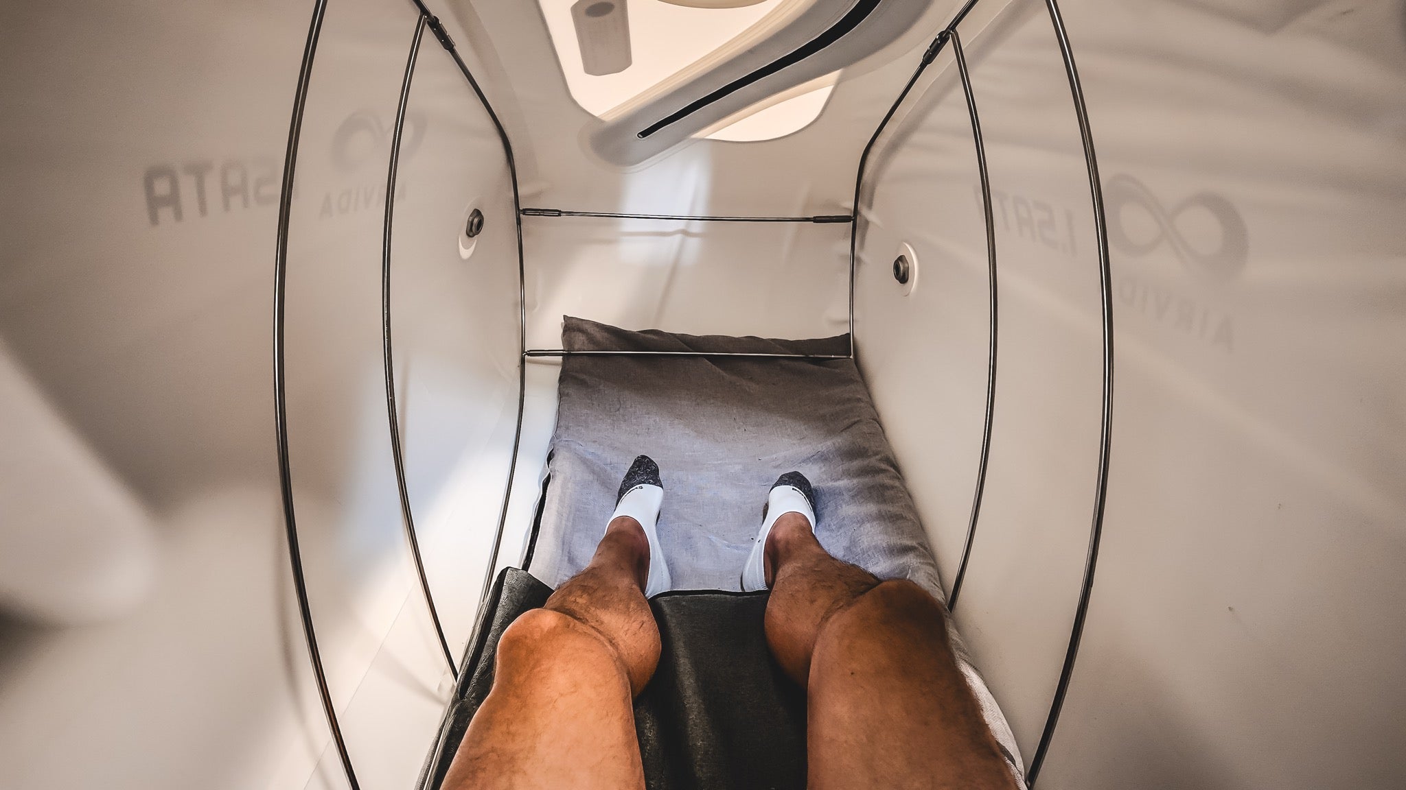 An AIRVIDA hyperbaric chamber with a person lying comfortably inside, showing padded bedding, support frame, and viewing windows.