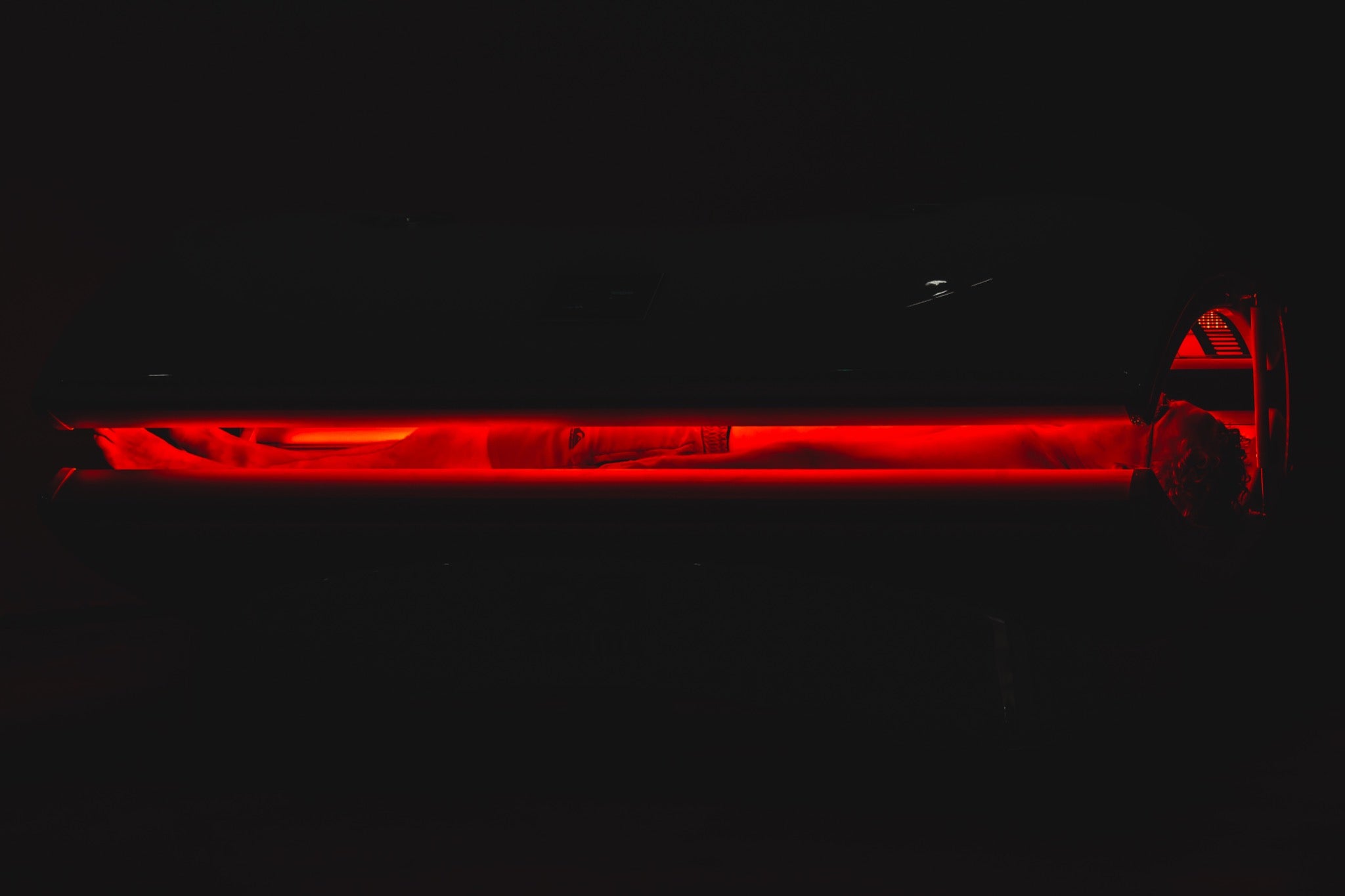 Person receiving full-body red light therapy inside a closed light therapy bed with red LED illumination.