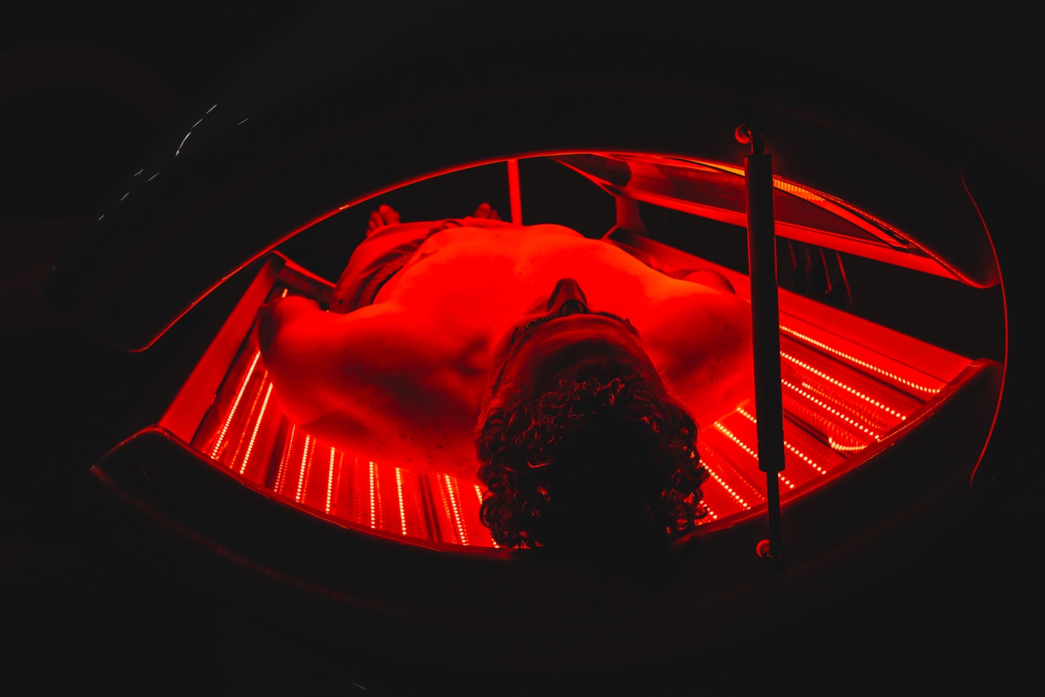 Man lying inside an AIRVIDA red light therapy bed, surrounded by intense red LED illumination designed to provide full-body light exposure.