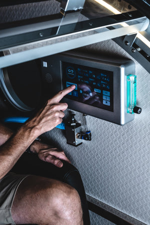 Person adjusting the touchscreen control panel inside a hard-shell hyperbaric chamber during an HBOT session.