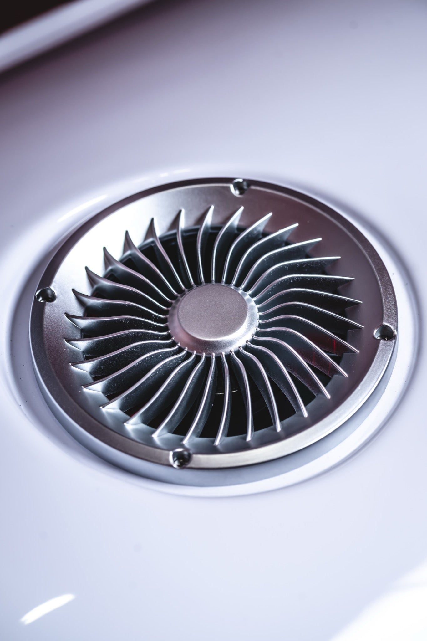 Close-up of a circular metallic ventilation outlet, securely mounted on the smooth white surface of an AIRVIDA unit.