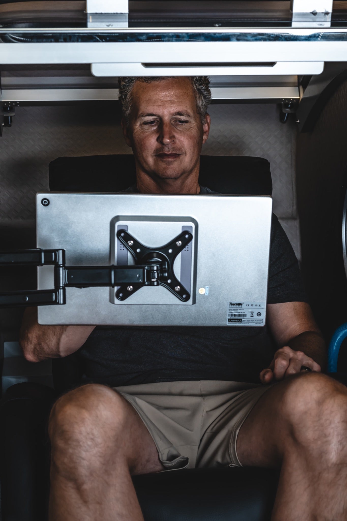 Man seated inside a hard-shell hyperbaric chamber while using an adjustable monitor during an HBOT session.