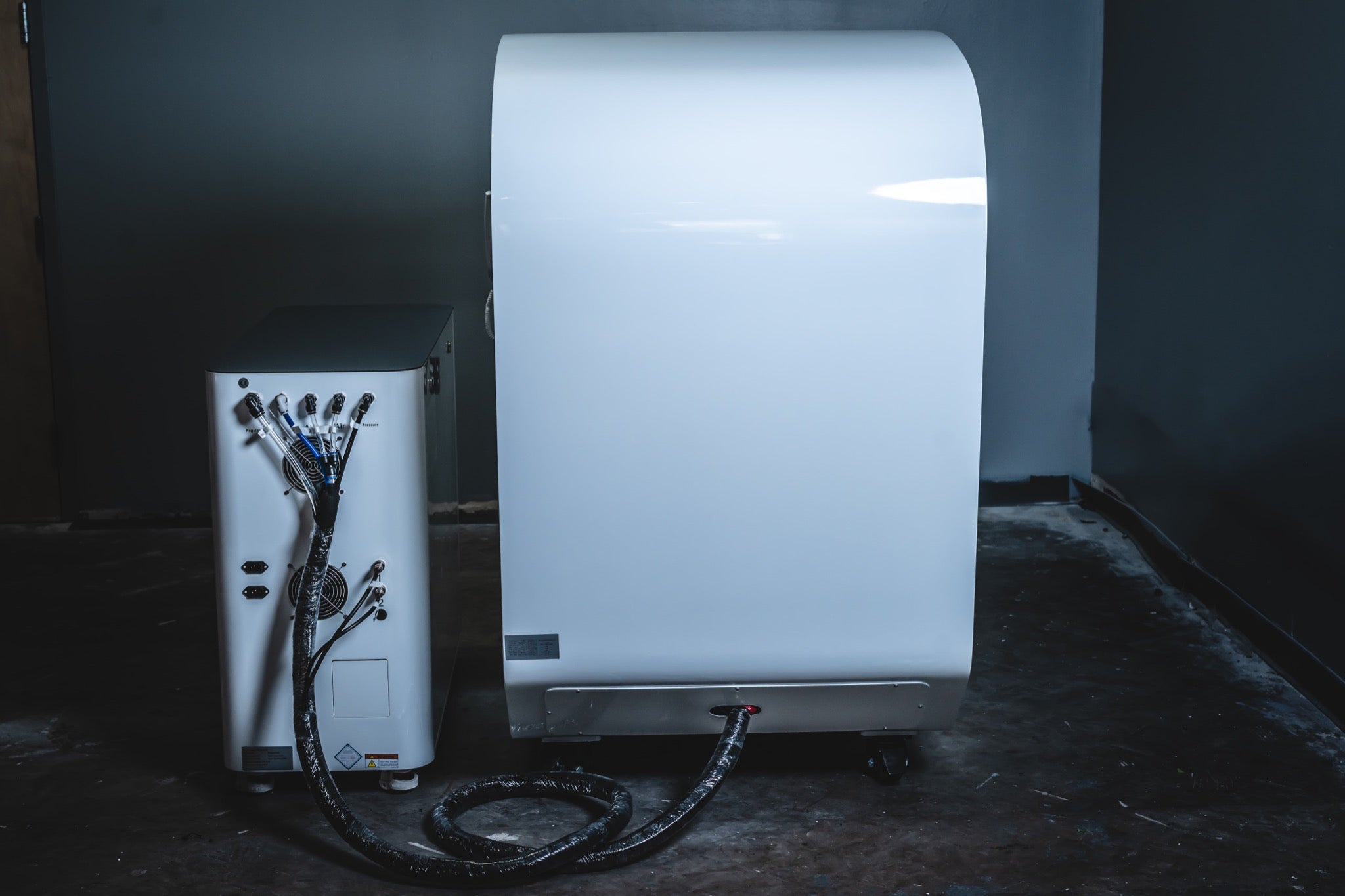 Rear view of a hard-shell hyperbaric chamber connected by hoses to its external oxygen and control system unit.