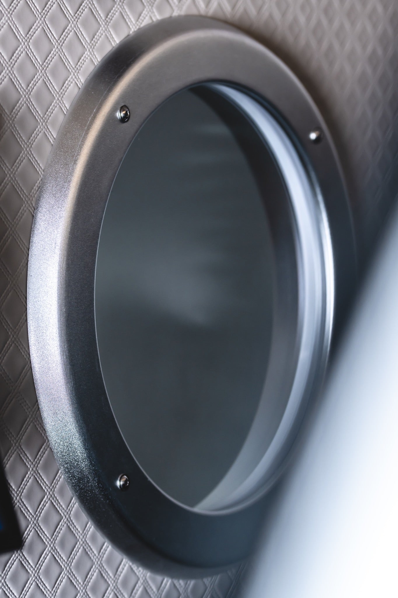 Close-up of a circular viewing window inside a hard-shell hyperbaric chamber with a quilted interior wall.