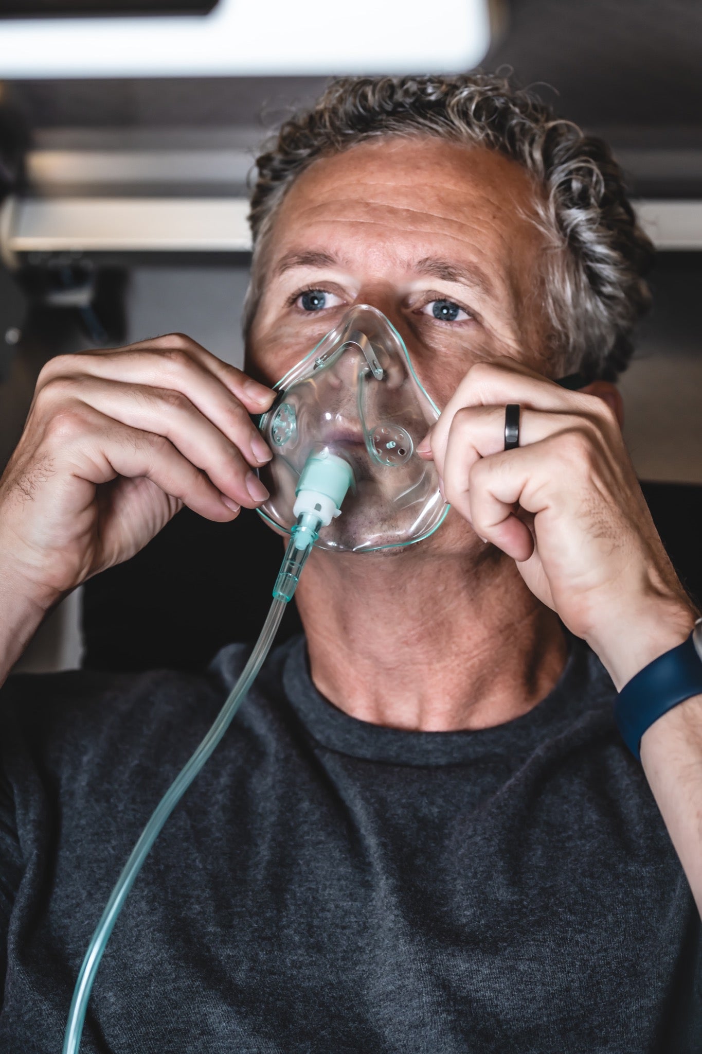 Man adjusting a clear oxygen mask while seated inside a hyperbaric chamber during an HBOT session.