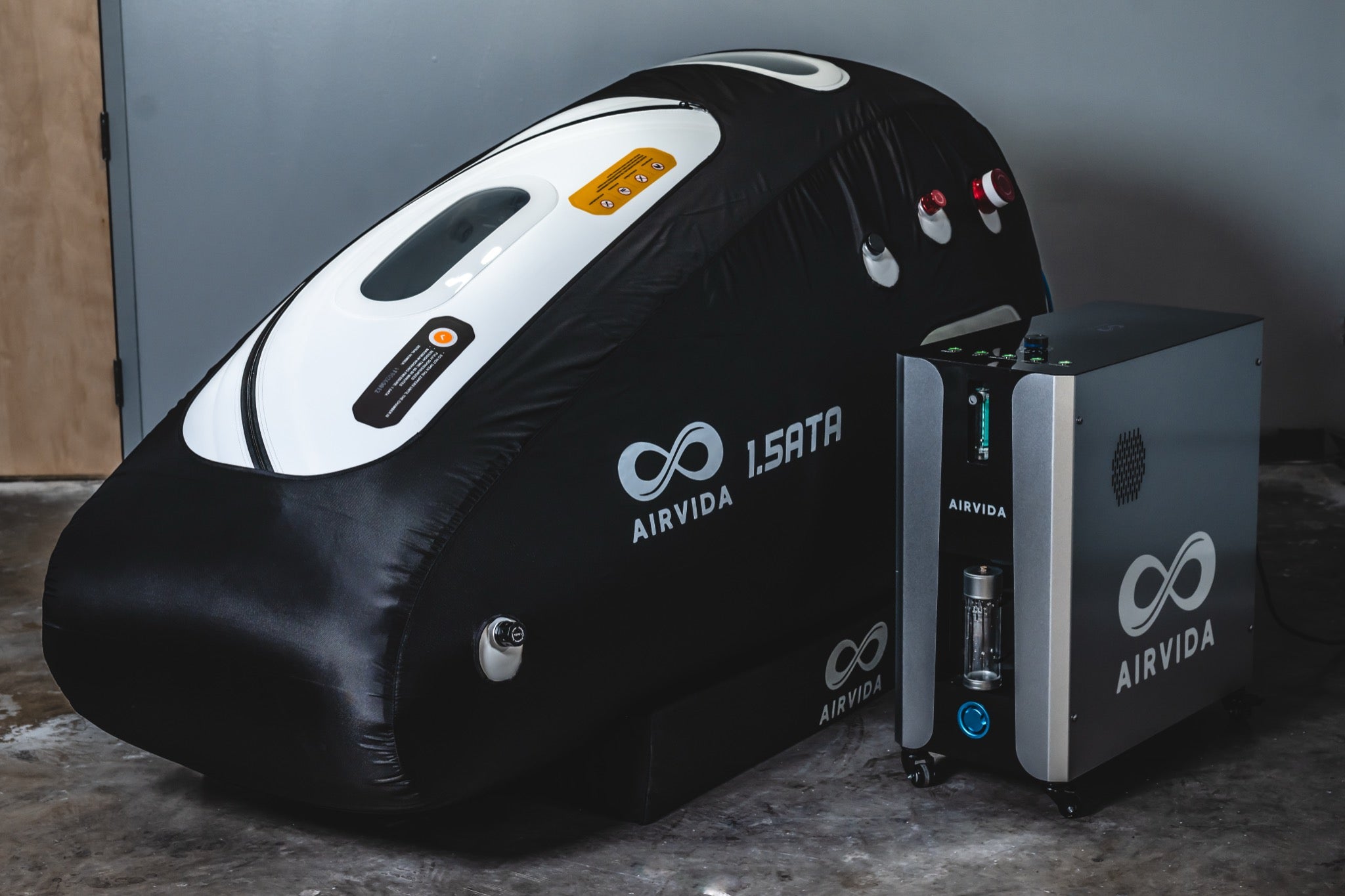 AIRVIDA 1.5 ATA soft-shell hyperbaric chamber with viewing windows, pressure valves, and a separate oxygen concentrator unit positioned beside it.