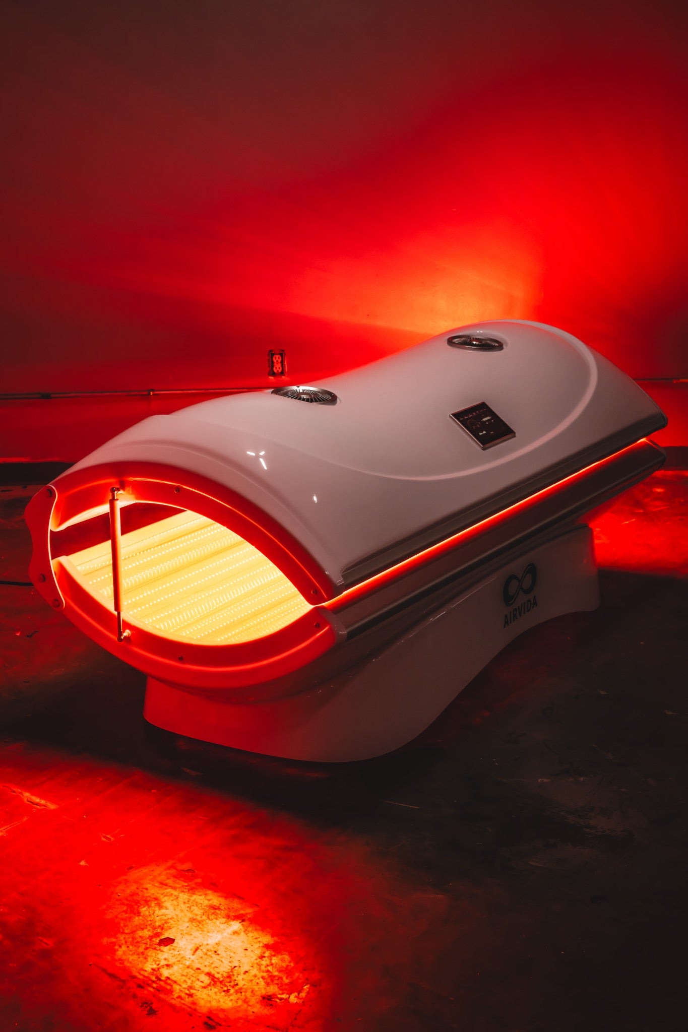 AIRVIDA red light therapy bed glowing with bright red LEDs in a dark room, featuring a sleek white canopy, touchscreen, and full-body design.
