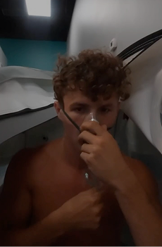 Person sitting inside a hyperbaric chamber, holding an oxygen mask over their nose, with medical tubing visible.