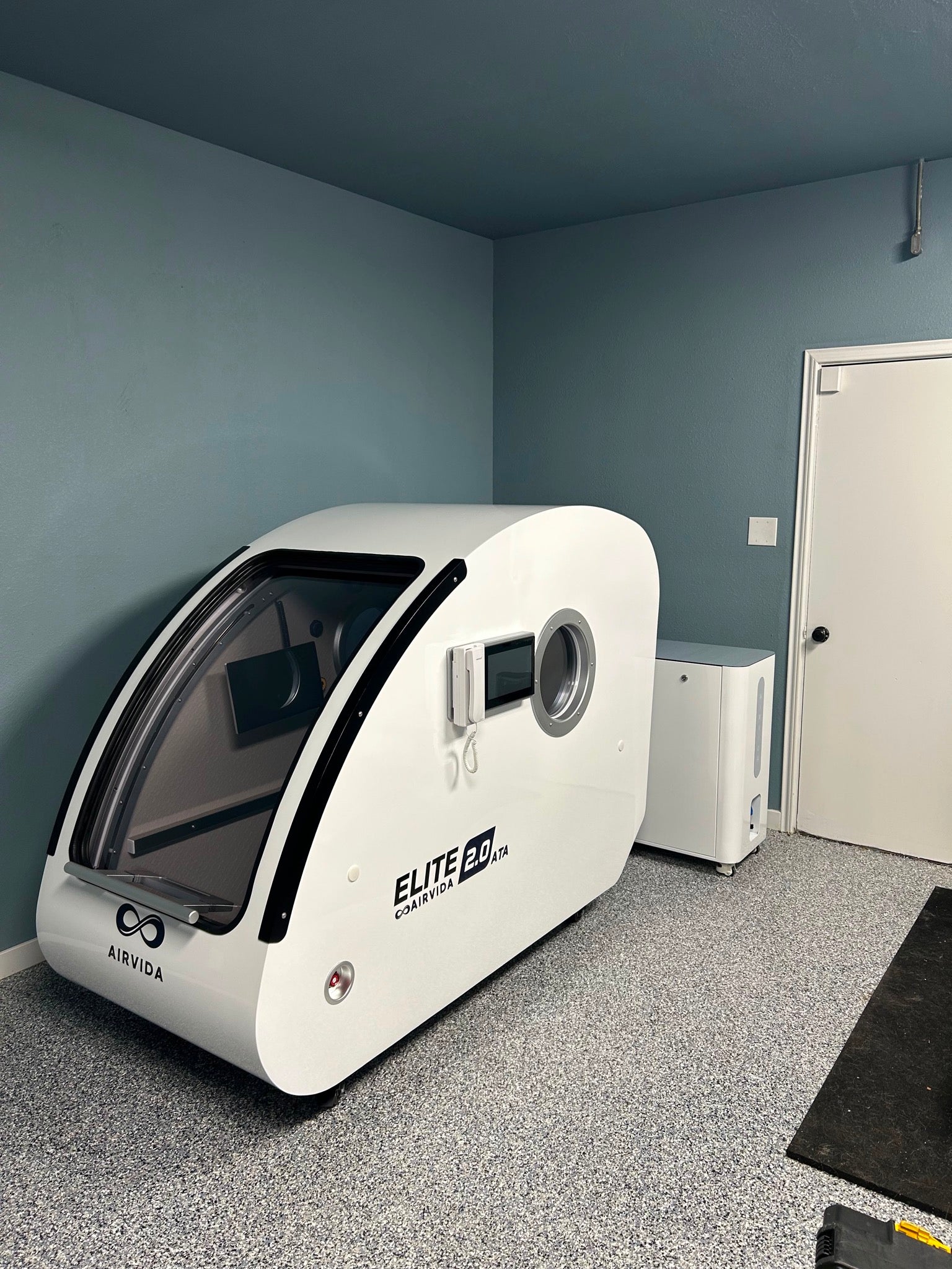 Airvida Elite 2.0 ATA hard-shell hyperbaric chamber with control panel and oxygen system installed in a treatment room.