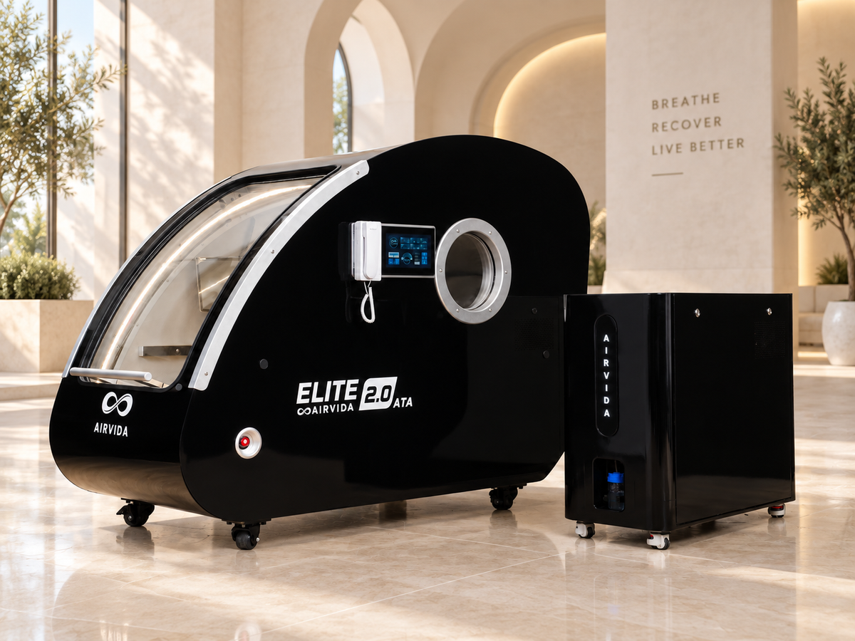 Black Airvida Elite 2.0 ATA hyperbaric chamber with touchscreen and oxygen system displayed in a bright luxury wellness room with arched walls and plants.