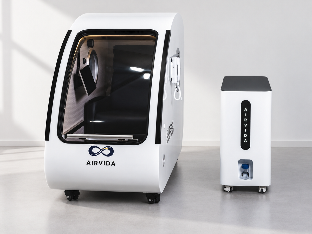 White Airvida hyperbaric chamber with clear curved door, black cushioned seat and matching oxygen unit on wheels, displayed in a bright modern wellness room.
