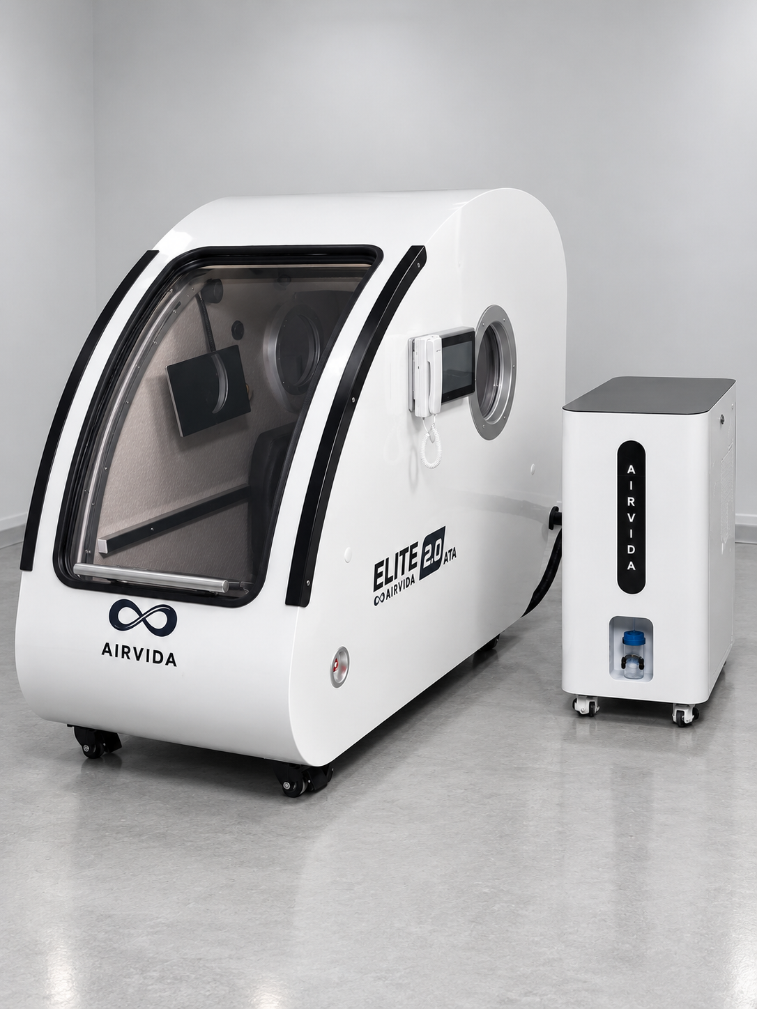 White Airvida Elite 2.0 ATA hyperbaric chamber with clear curved door, digital controls and matching oxygen unit on wheels in a clean modern wellness room.