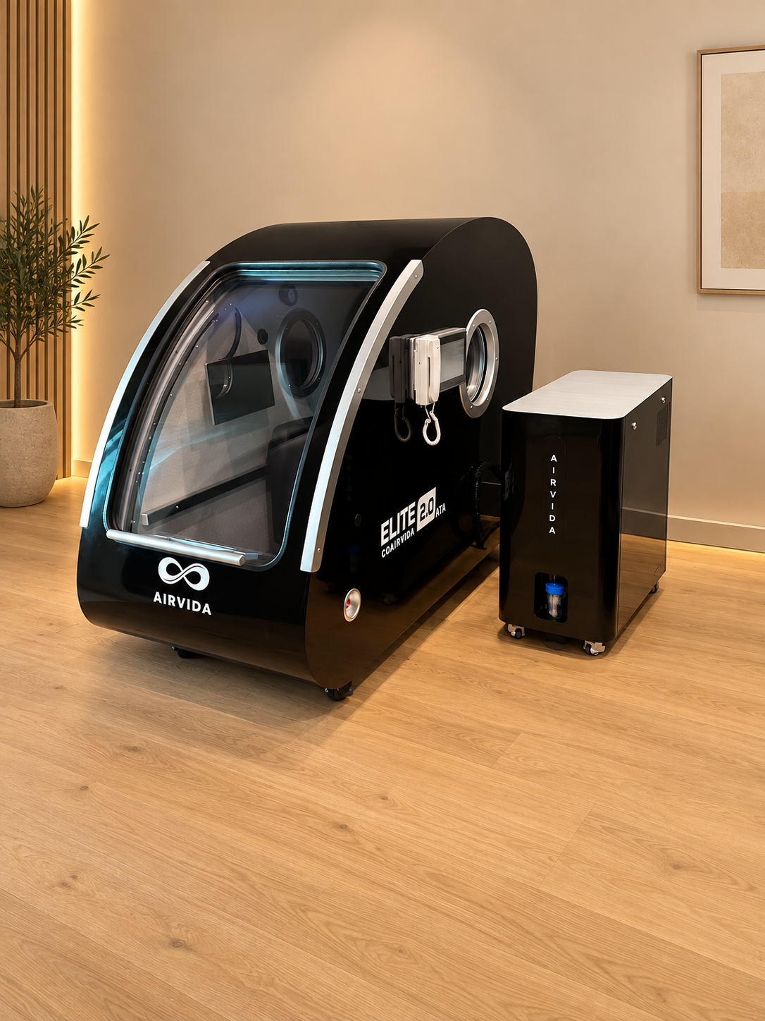 Black Airvida Elite 2.0 hyperbaric chamber with matching oxygen system, clear front door and controls displayed in a warm modern room with wood flooring.