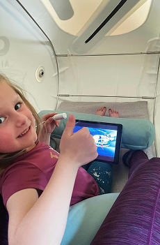 Child lying comfortably inside a hyperbaric chamber, giving a thumbs-up while watching a movie on a tablet during a therapy session.