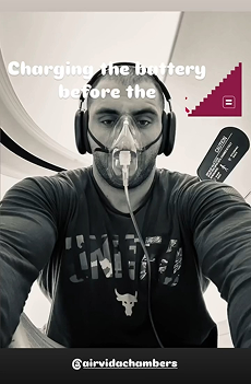 Man wearing an oxygen mask and headset inside a hyperbaric chamber, preparing equipment while seated during a therapy session.